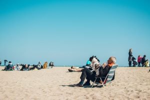 An older man resting on the beach with his dog sitting in his lap