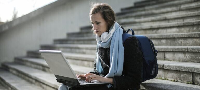A female student sitting at the steps of a building and working on her laptop.