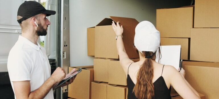 A man and a woman with caps looking at cardboard boxes.