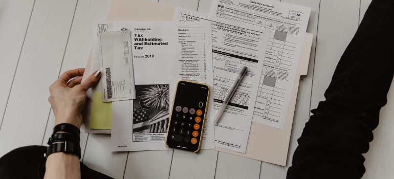 A hand with tax paper and a calculator on the table surface.