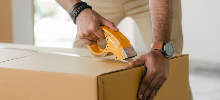 a man putting moving tape on a cardboard box when moving from Miami to Denver