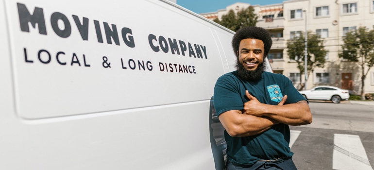 A mover employee smiling next to their van while answering questions to ask movers before an interstate move