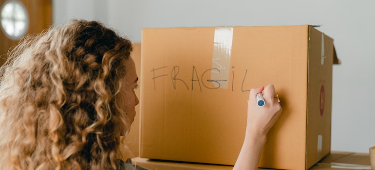 A woman writing a note on a carton box with a marker.