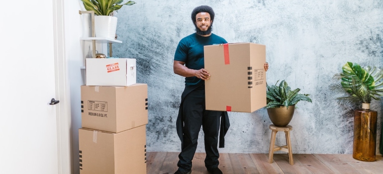 a professional moving crew personnel standing in the room with cardboard boxes around him to depict one of many processes in the PCS move process