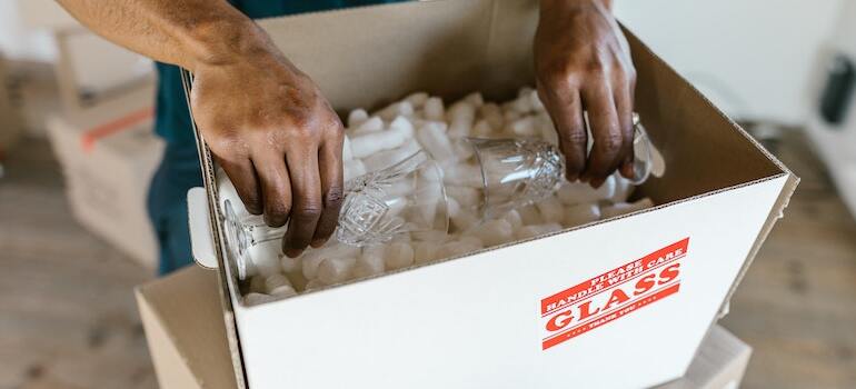 A mover packing a glass inside a moving box full of packing peanuts