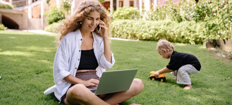 a woman sitting on grass with a laptop talking on the phone