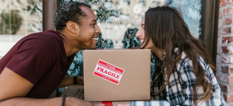 A man and woman moving with a moving box with a 'fragile' sticker on it