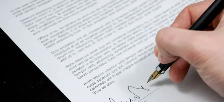 A person using a pencil to sign and read a lease agreement