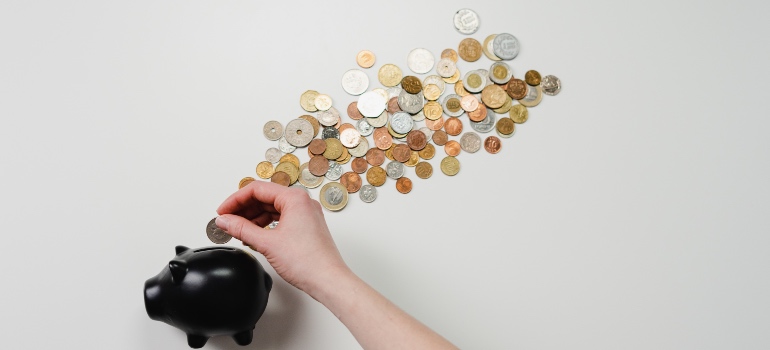 A person putting coins in a black piggy bank
