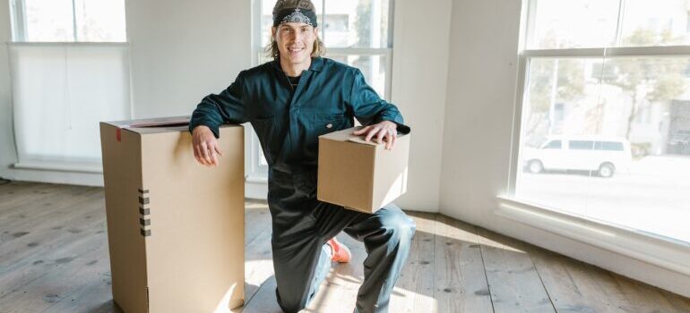 A mover from best cross country movers Renton holding a box in one hand while leaning on another box