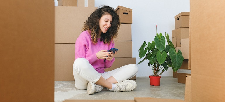 a woman sitting on the floor and looking for temporary housing during the move on a cell phone