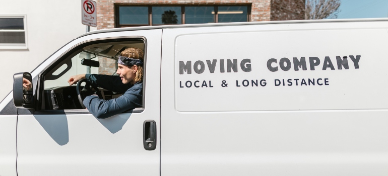 A man with blond hair driving a white moving van