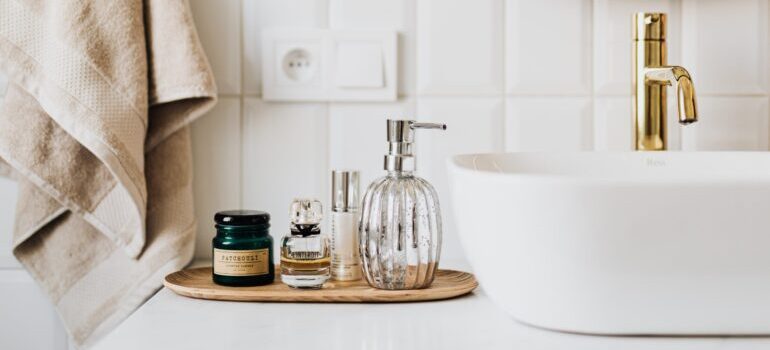 Glass supplements, perfume and soap dispenser on the bathroom counter with golden fixtures on a counter top sink