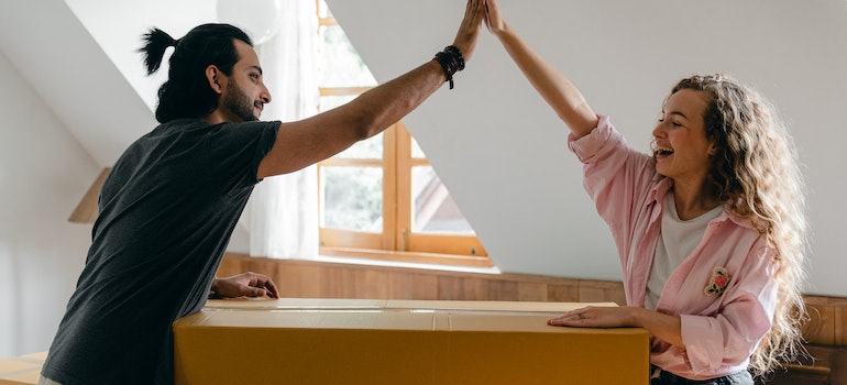 Two persons greeting by giving high fives over a cardboard box