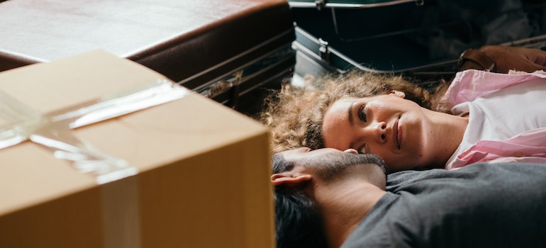 a couple talking while laying on the floor with packed cardboard boxes and suitcases