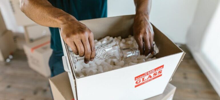 A mover packing crystal glasses in a box filled with packing peanuts and a label saying "glass" on it