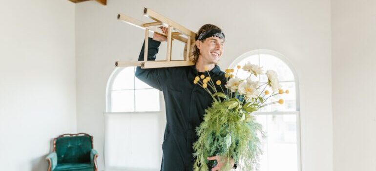 mover from the best cross country movers Beaverton carrying a wooden stool and a vase with yellow flowers