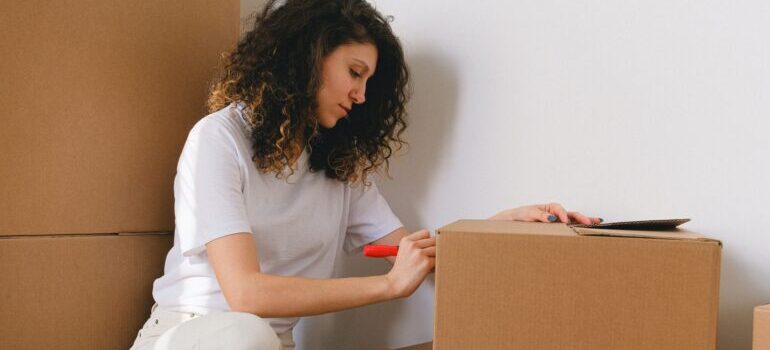 Woman writing on a box and thinking about DIY vs. hiring professionals for a move