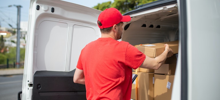 A mover in red taking boxes from a white van