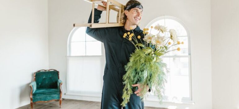 A mover holding a chair and flowers during the move