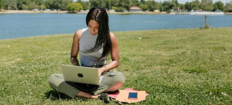Woman sitting on the grass and using her laptop to look up tips for a successful international relocation