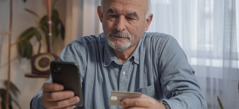 an older man in a blue shirt looking at his phone while holding a visa card