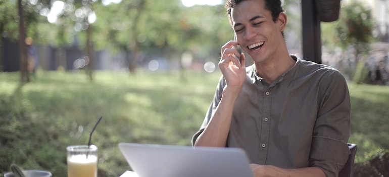 A man smiling while using his laptop and phone