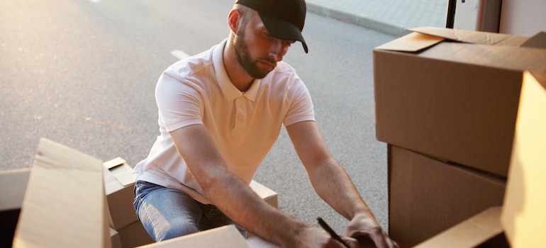 man working for efficient moving companies writing on a cardboard box