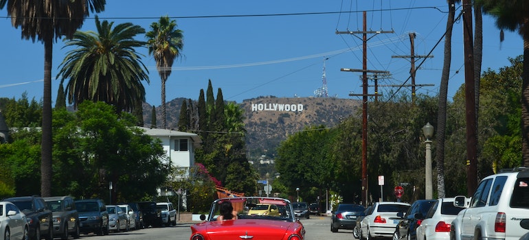 A person in a red car driving toward the Hollywood sign after reading about the moving trends in California