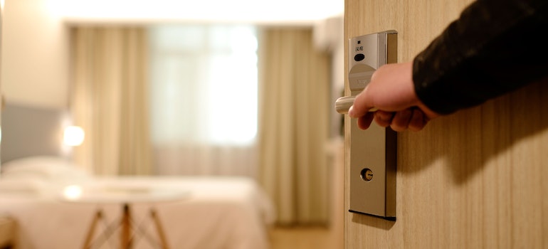 person holding a handle and opening a wooden door to a bedroom