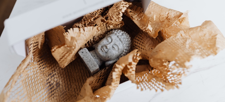 Person packing an antique Buddha head in paper after learning how to pack heirlooms