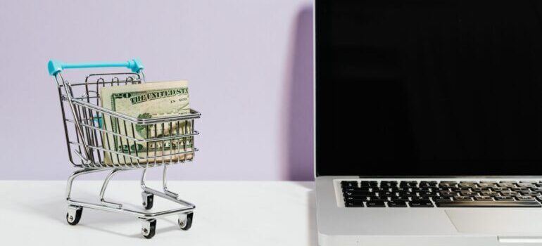 Small shopping cart with money in it next to a laptop