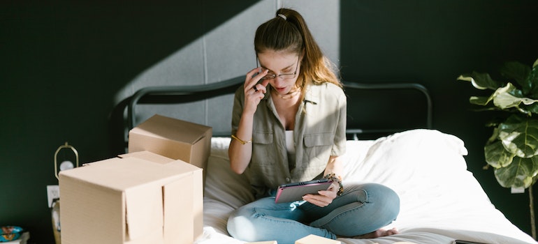 a young woman sitting on the bed and reading on a cell phone about sustainable office move