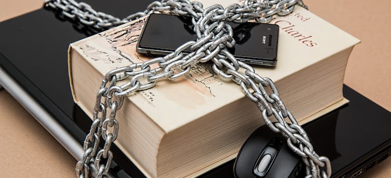 a cell phone, and a book over a laptop wrapped in chains