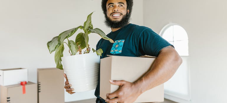 a man holding a moving box and a plant 