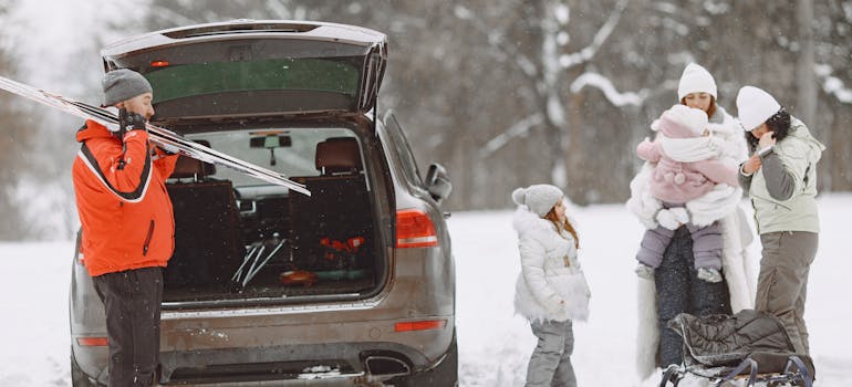 A man unloading skis out of a car while explaining how to transport winter sports gear and equipment to his family.