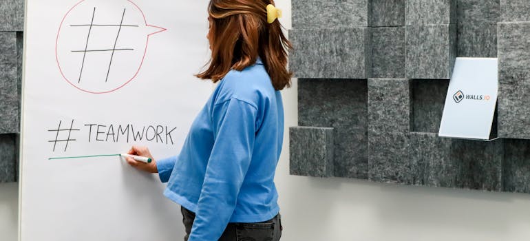 A woman in blue writing on a board plan for how to include employees in an office relocation