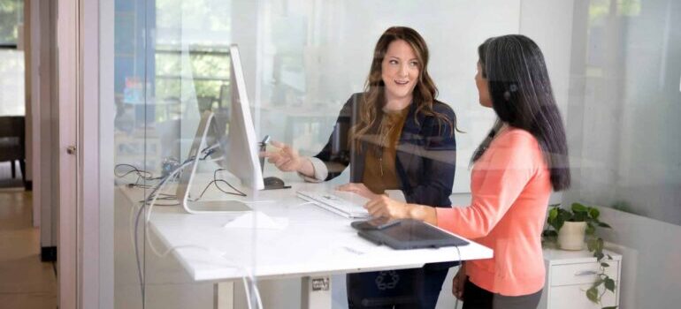 Two women standing next to a computer and talking about reasons to move to Atlanta
